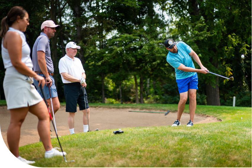 one golfer hitting while teammates watch at Cardinal Legacy Golf Outing